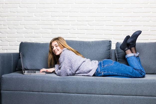 Chica adolescente feliz en línea con un portátil acostado en la cama en la sala de estar en casa