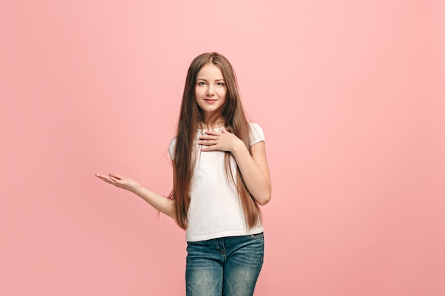 Chica adolescente feliz de pie y presentando algo, sonriendo aislado en la pared rosa de moda. Hermoso retrato femenino de medio cuerpo. Las emociones humanas, el concepto de expresión facial.