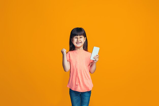 La chica adolescente feliz de pie y sonriendo contra naranja.