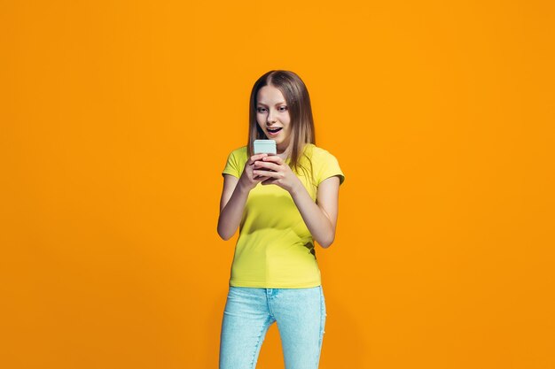 La chica adolescente feliz de pie y sonriendo contra naranja.