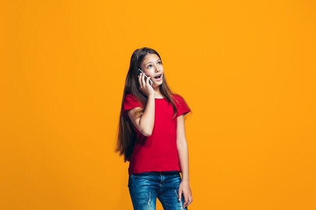 La chica adolescente feliz de pie y sonriendo contra naranja.