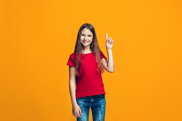 La chica adolescente feliz de pie y sonriendo contra naranja.