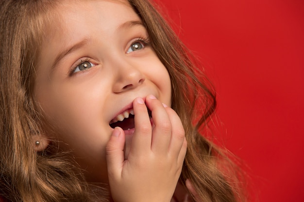 La chica adolescente feliz de pie y sonriendo sobre fondo rojo.