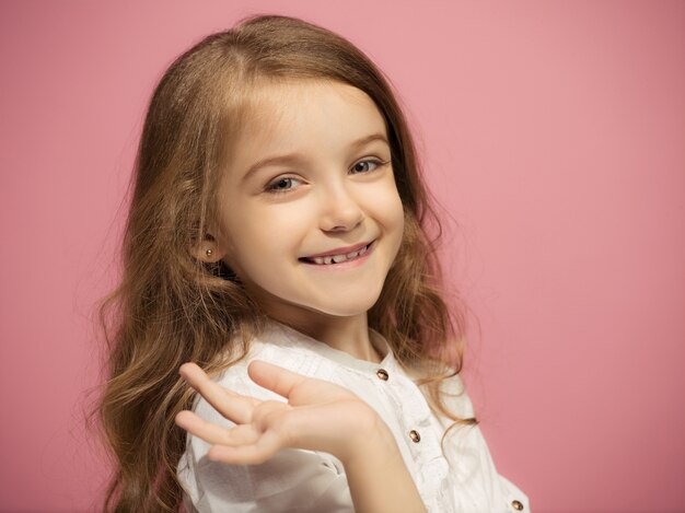 La chica adolescente feliz de pie y sonriendo sobre fondo rosa.