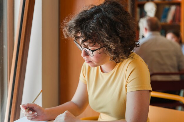 Foto gratuita chica adolescente con gafas estudiando cerca de la ventana