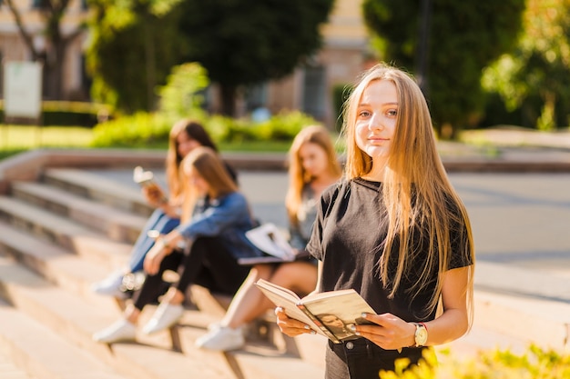 Chica adolescente con libro cerca de amigos