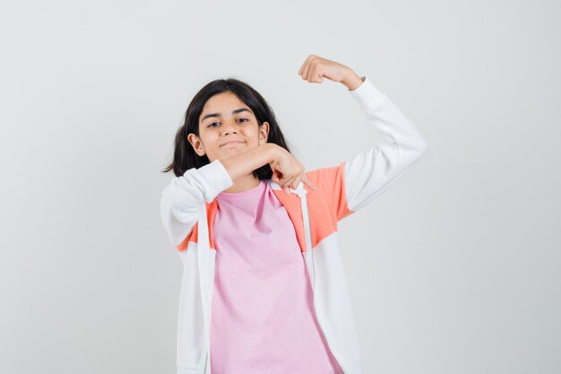 Chica adolescente mostrando su músculo del brazo en chaqueta, camisa rosa y luciendo jactanciosa.