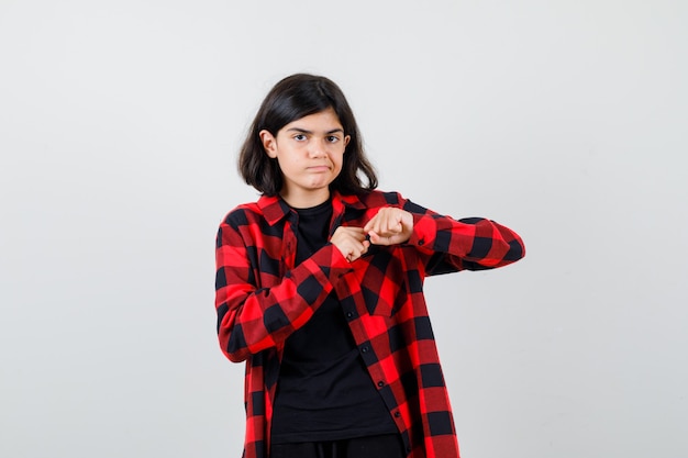 Chica adolescente de pie en pose de lucha en camiseta, camisa a cuadros y mirando imprudente. vista frontal.