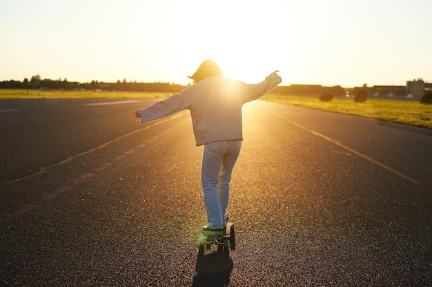 Chica adolescente sintiéndose feliz en longboard feliz joven patinadora montando su patineta con las manos extendidas