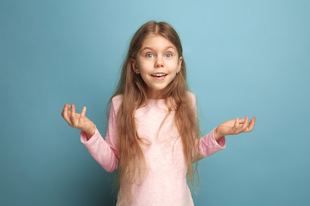 chica adolescente sorprendida sobre un fondo azul de estudio. Expresiones faciales y concepto de emociones de personas.