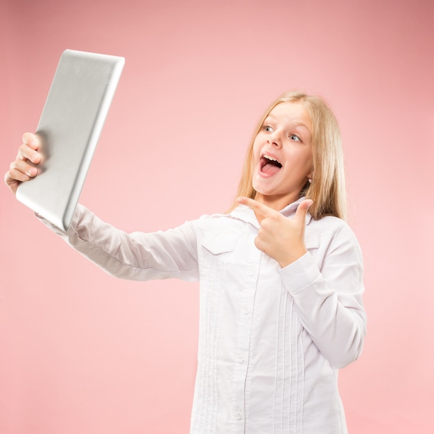 Chica adolescente con una tableta. Retrato frontal de medio cuerpo femenino atractivo, fondo de color rosa moderno de estudio.