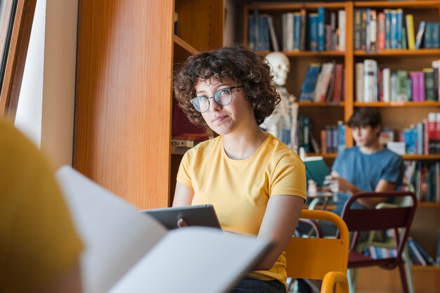 Chica adolescente con tableta sentado en la biblioteca