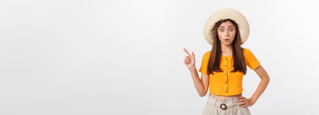 Chica adolescente en vacaciones de verano sorprendida y señalando con el dedo en el espacio de copia sobre bac blanco aislado