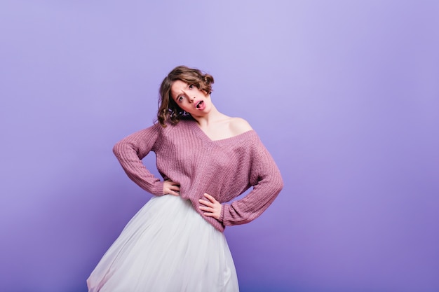 Chica adorable emocional con cabello oscuro y rizado posando en falda larga de moda. Linda mujer caucásica viste camisa púrpura suave bailando