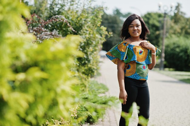 Chica afroamericana en camisa de color y pantalón negro posó al aire libre