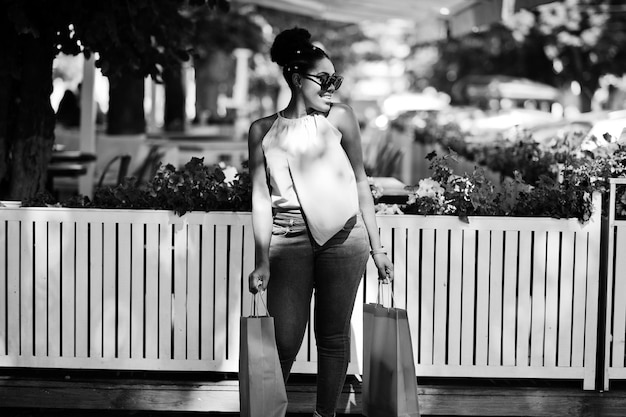 Chica afroamericana casual con bolsas de compras de colores caminando al aire libre Elegante mujer negra de compras