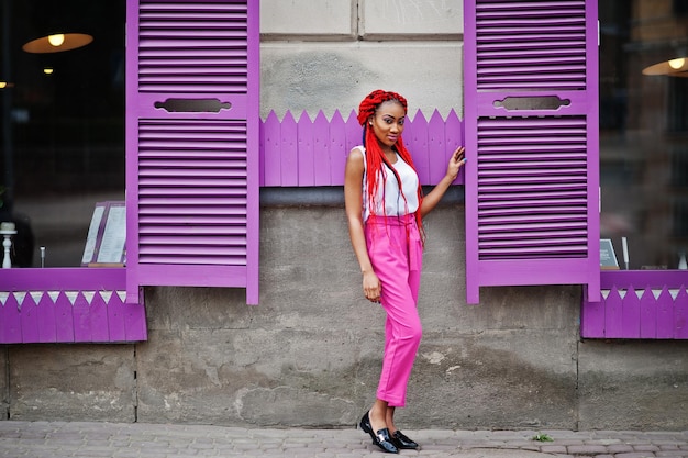 Foto gratuita chica afroamericana de moda en pantalones rosas y rastas rojas posadas al aire libre