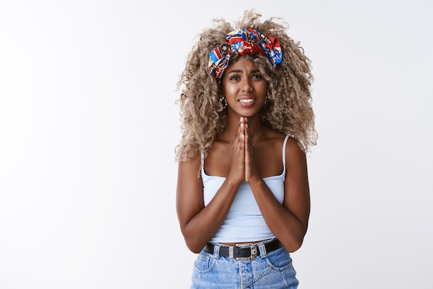 Foto gratuita chica afroamericana pidiendo favor quiere prestar dinero suplicando ayuda tomarse de la mano en oración sonriendo incómodo y preocupado frunciendo el ceño suplicando disculpas decir lo siento como fondo blanco de pie