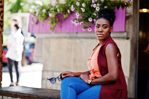 Chica afroamericana sentada al aire libre con gafas de sol en las manos