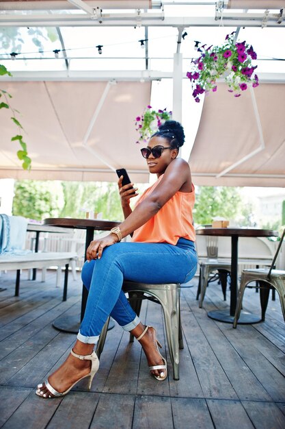 Chica afroamericana sentada en la mesa de café con teléfono móvil