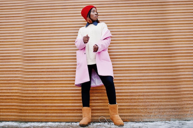 Chica afroamericana con sombrero rojo y abrigo rosa contra persianas naranjas