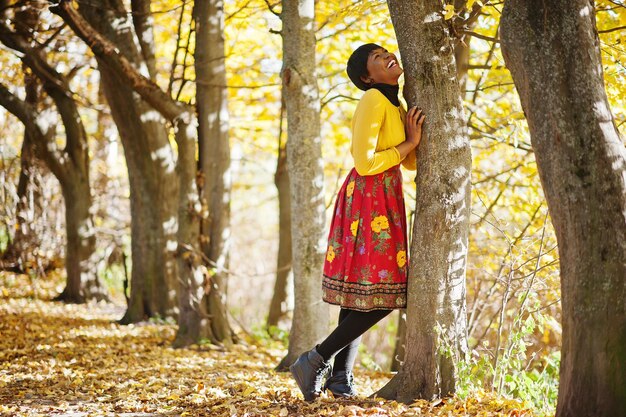 Chica afroamericana en vestido amarillo y rojo en el parque de otoño dorado