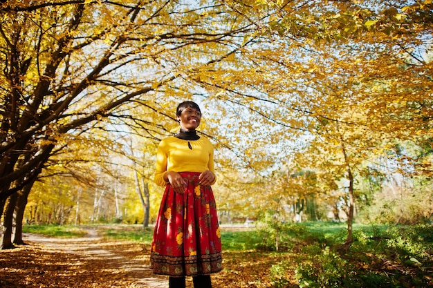 Chica afroamericana en vestido amarillo y rojo en el parque de otoño dorado