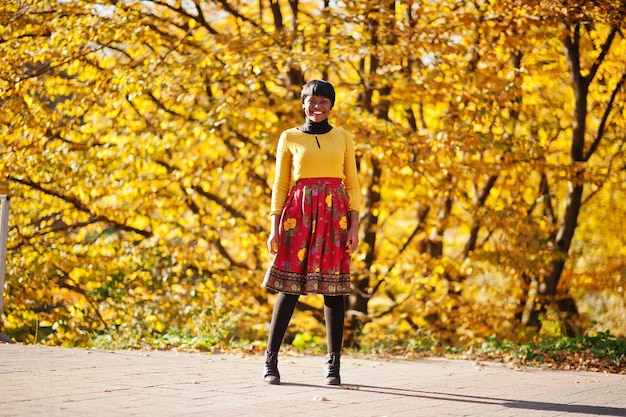 Chica afroamericana en vestido amarillo y rojo en el parque de otoño dorado