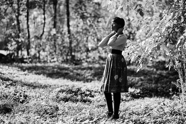 Chica afroamericana en vestido amarillo y rojo en el parque de otoño