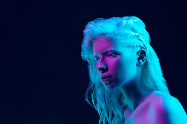 Chica albina con piel blanca, labios naturales y cabello blanco en luz de neón aislada sobre fondo negro de estudio.