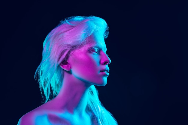 Chica albina con piel blanca, labios naturales y cabello blanco en luz de neón aislada sobre fondo negro de estudio.