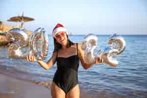Foto gratuita chica alegre con bolas de plata en forma de números 2022 cerca del concepto de mar de año nuevo