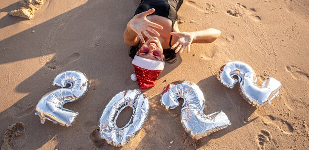 Chica alegre con bolas de plata en forma de números 2022 cerca del concepto de mar de Año Nuevo