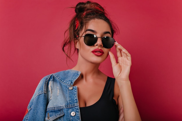 Chica alegre bronceada con accesorios vintage posando en gafas de sol negras