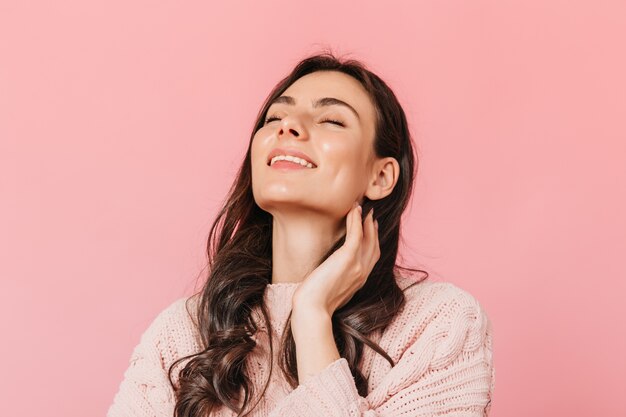 Chica alegre con cabello oscuro ondulado posa con sonrisa y ojos cerrados sobre fondo aislado.