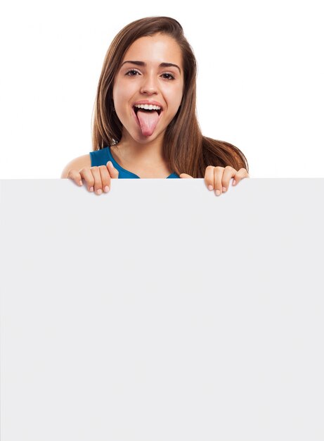 Chica alegre enseñando la lengua y sujetando un cartel vacío