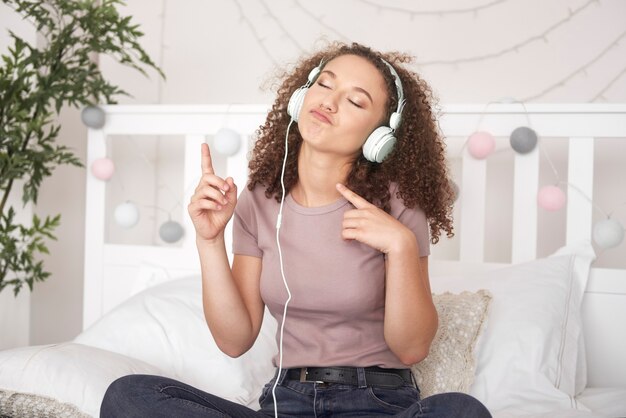 Chica alegre escuchando música y bailando en la cama