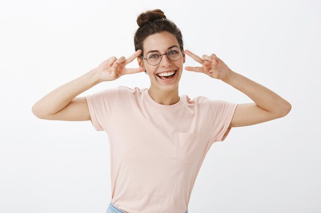 Chica alegre con gafas posando contra la pared blanca
