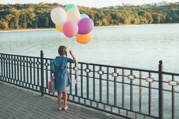 Chica alegre con globos de colores y maleta infantil