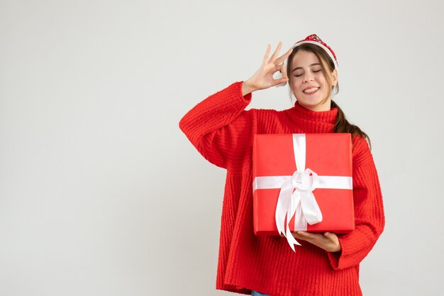 Chica alegre con gorro de Papá Noel haciendo okey firmar en blanco