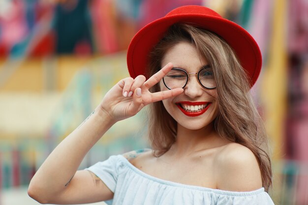 Chica alegre guiñando un ojo y sonriendo mientras muestra el signo de la victoria