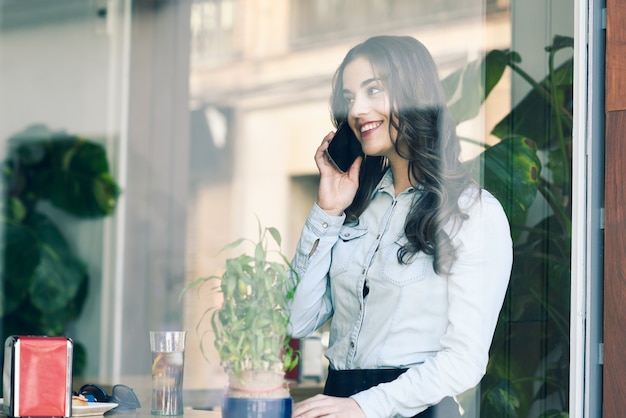 Chica alegre hablando por teléfono en un restaurante