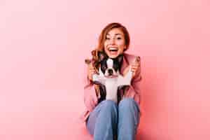 Foto gratuita chica alegre en jeans jugando con perrito gracioso. retrato interior de dama jengibre emocionada con peinado rizado pasar tiempo con su cachorro.