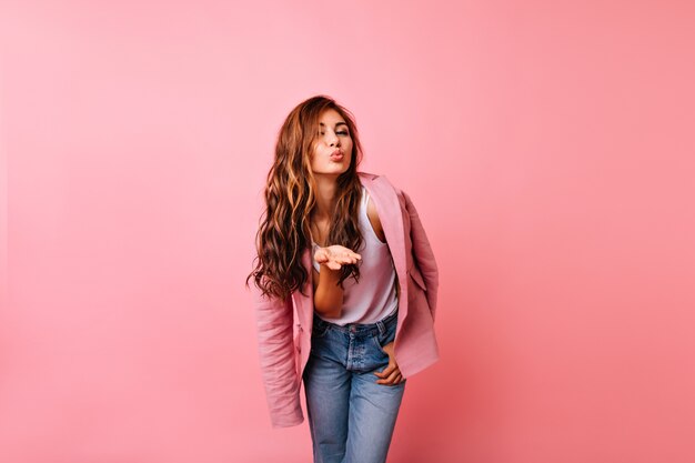 Chica alegre en jeans posando con expresión de cara de besos. Atractiva dama pelirroja enviando beso al aire.