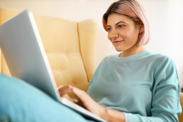 Chica alegre jugando juegos de video en línea a través de la computadora portátil.