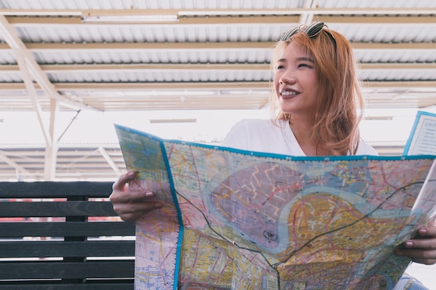 Chica alegre con mapa en la estación de tren