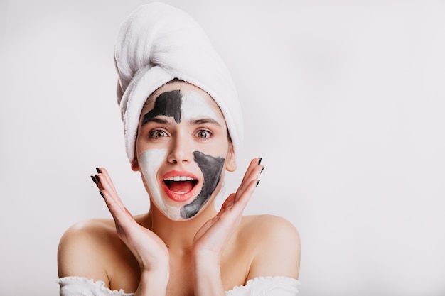 Chica alegre con mascarilla de sorpresa. Mujer de ojos verdes posando en la pared blanca después de lavarse el pelo.