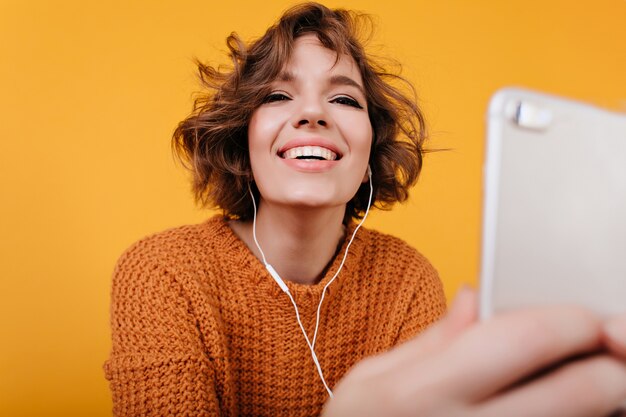 Chica alegre con peinado ondulado escuchando música en auriculares