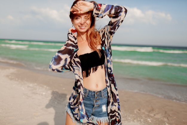 Chica alegre pelirroja posando en la playa soleada.