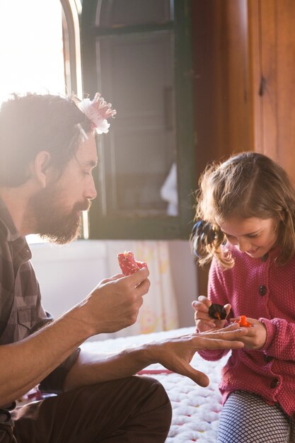 Chica alegre pintando las uñas del padre